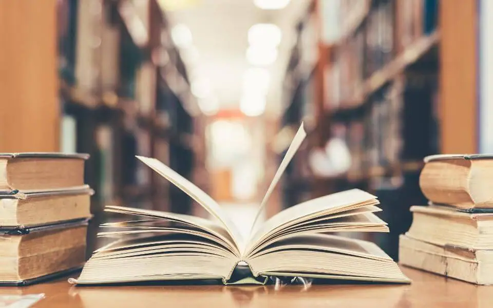 open book on a table with stack of books on both sides with book shelves in background