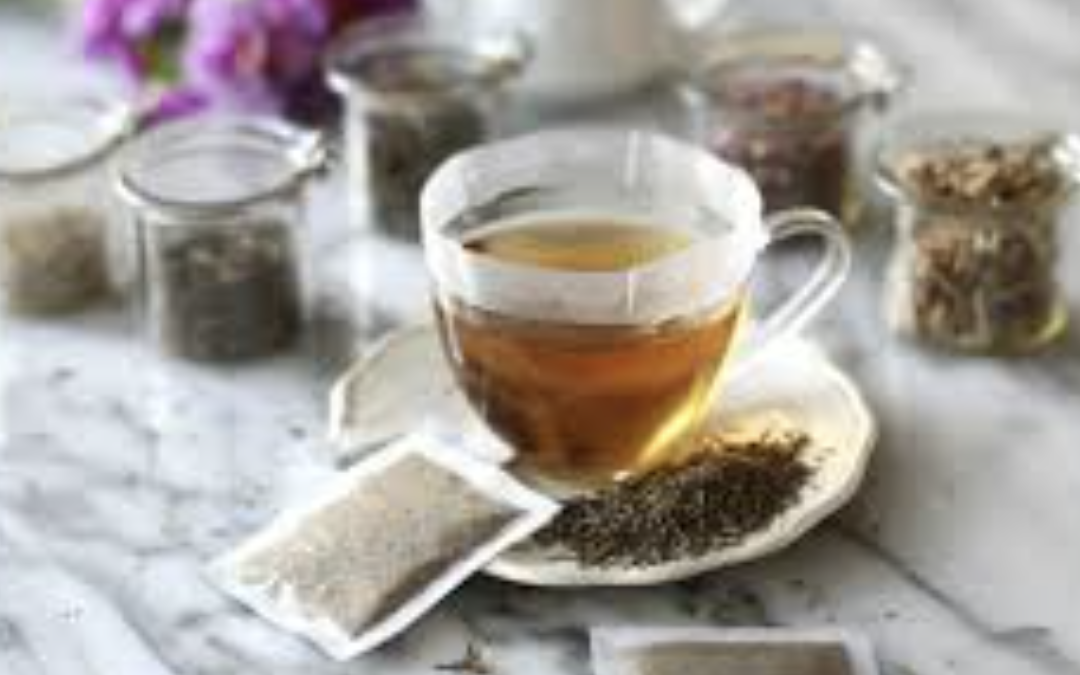 Glass cup with tea, surrounded by jars of tea and spices on a marble surface.