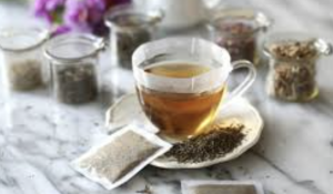 Glass cup with tea, surrounded by jars of tea and spices on a marble surface.